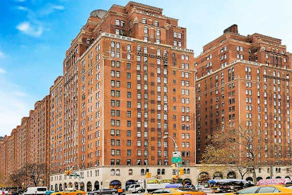 A large red brick building with many windows in the middle of a city street.
