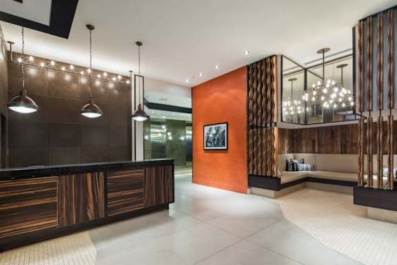 A modern office lobby with a wooden reception desk and a glass wall. at The Maximilian Apartments, Long Island City, 11101