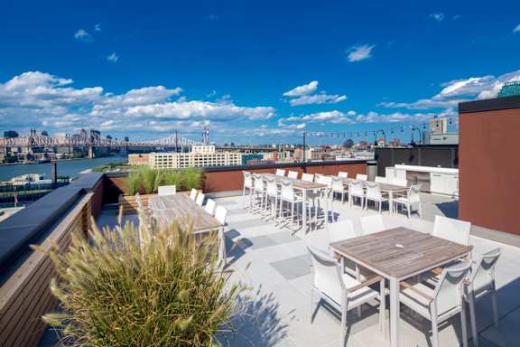 A rooftop patio with a table and chairs overlooking a city skyline. at The Maximilian Apartments, New York