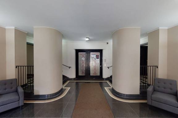 A hallway with a brown carpet and grey couches.