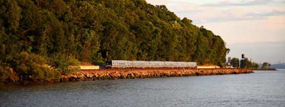 A train is on a track that runs along the edge of a body of water.