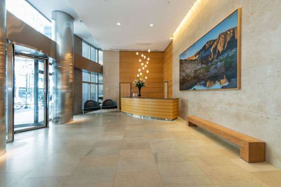 A large painting of a mountain landscape hangs on a wall above a wooden bench in a spacious lobby.
