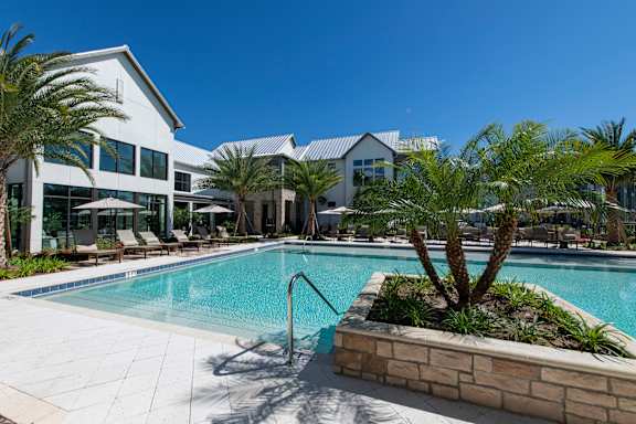 A pool surrounded by palm trees and a building in the background.