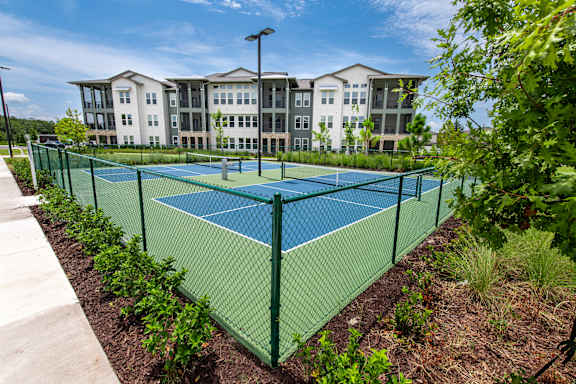A tennis court is surrounded by a green fence and vegetation.