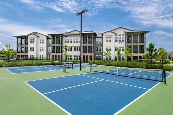 A tennis court in front of a large apartment building.