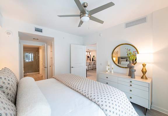 A bedroom with a bed, dresser, mirror, and ceiling fan.