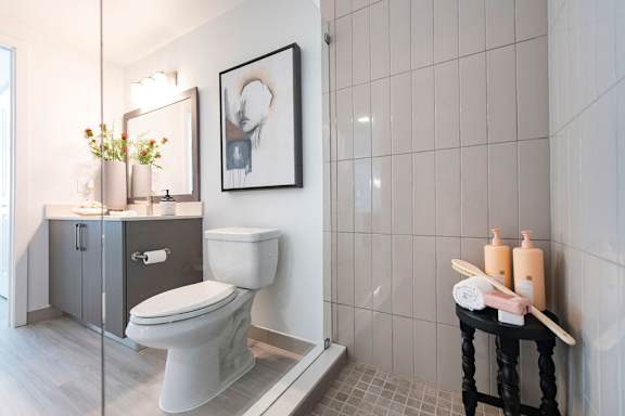 A white toilet sits in a bathroom with a black stool and a picture on the wall.