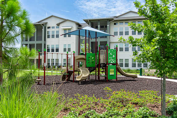 A playground with a green slide and red railings in front of a white building.