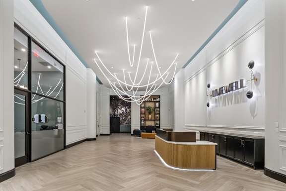 A reception area with a white reception desk and a large chandelier. at LiveWell Apartments, Pittsburgh