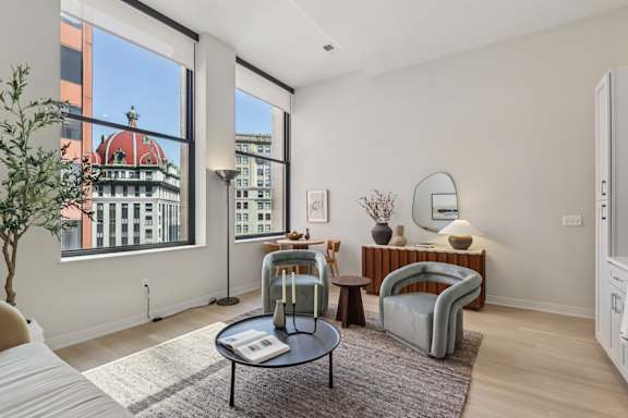 A living room with a large window and a view of a building with a red roof at LiveWell Apartments, Pittsburgh