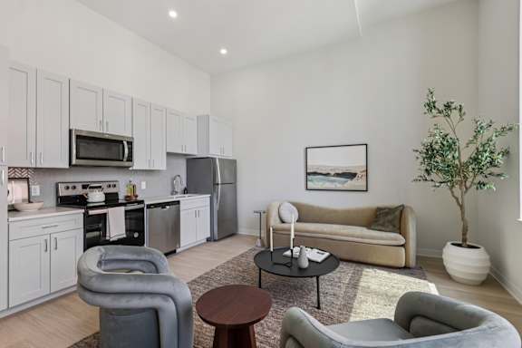 A modern living room with grey and white furniture and a kitchen area in the background. at LiveWell Apartments, Pennsylvania
