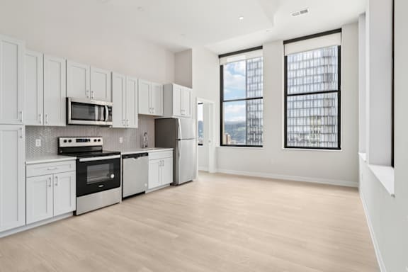 A kitchen with white cabinets and appliances, a wooden floor, and a view of the city through the windows. at LiveWell Apartments, Pittsburgh, PA
