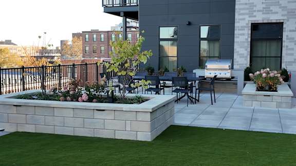 A patio with a table and chairs and a planter box with flowers. at The Pearl, Fort Wayne