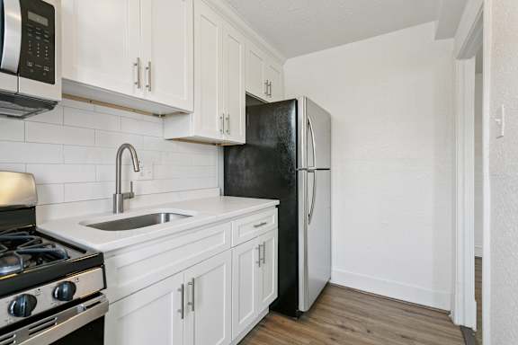 A black refrigerator is in a kitchen with white cabinets. at Shipyard Shores Apartments, Newport News