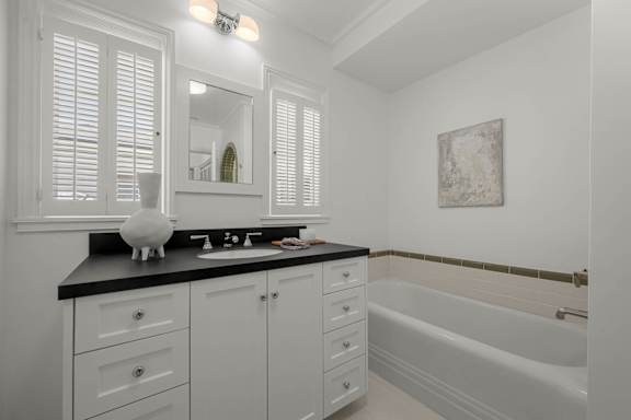 A white bathroom with a black countertop and a white bathtub.