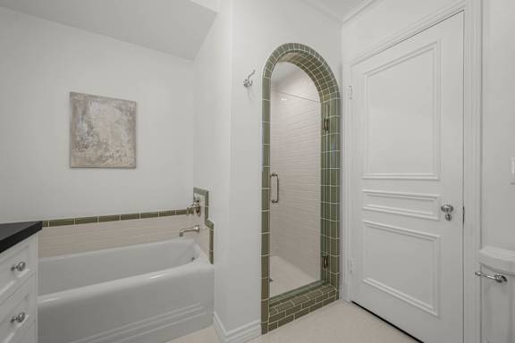 A white bathroom with a green tile archway shower.