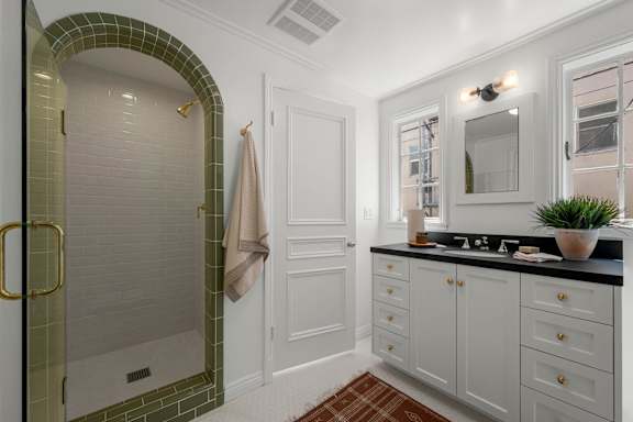 A bathroom with a green tiled shower and white cabinets.