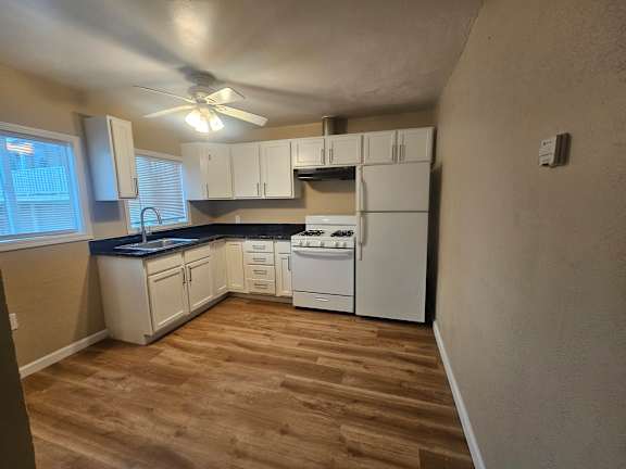 A kitchen with white appliances and wooden floors.