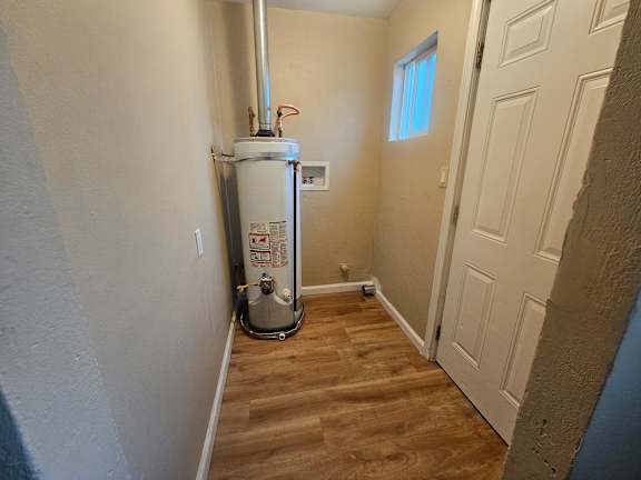 A wood floor leads to a white door in a room with a water heater.