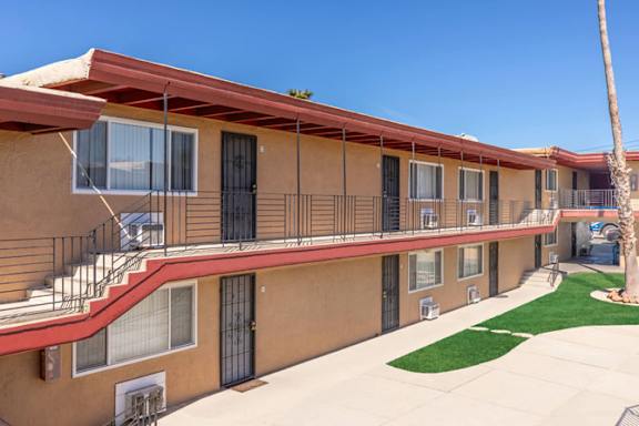 A row of apartment buildings with balconies and a palm tree in the front yard.
