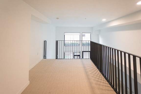 A room with a carpeted floor and a balcony with a railing.