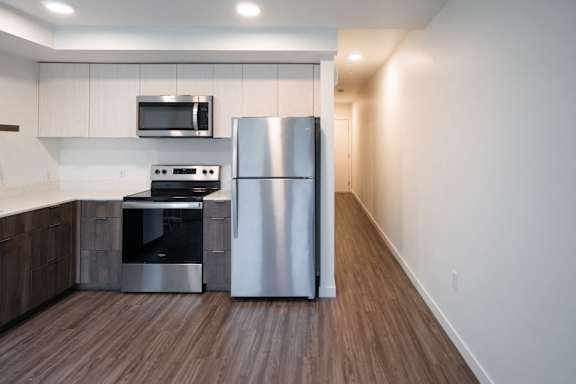 A modern kitchen with a stainless steel refrigerator and wooden flooring.