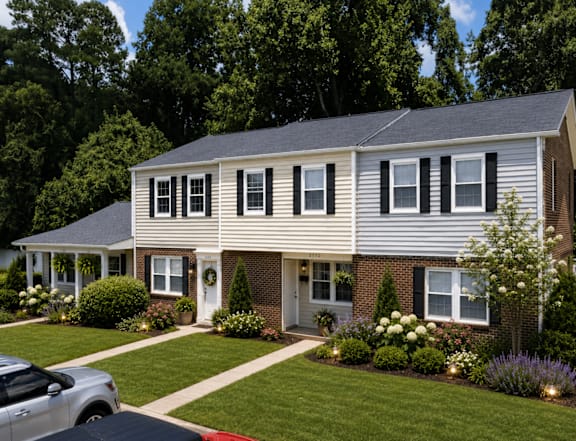A house with a grey roof and white siding with a red car parked in front.