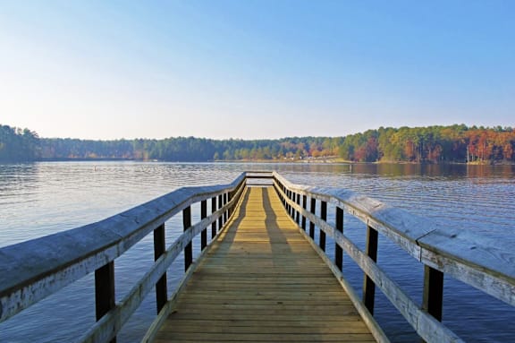 A wooden pier extends into a lake with trees in the background.