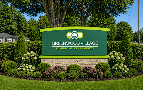 A sign for Greenwood Village Townhome Apartments is surrounded by a flower bed.