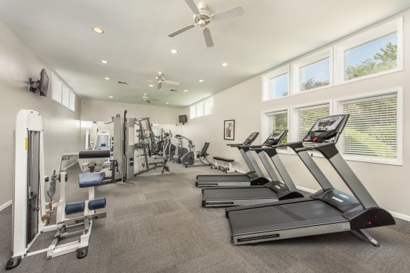 a gym with cardio machines and a ceiling fan