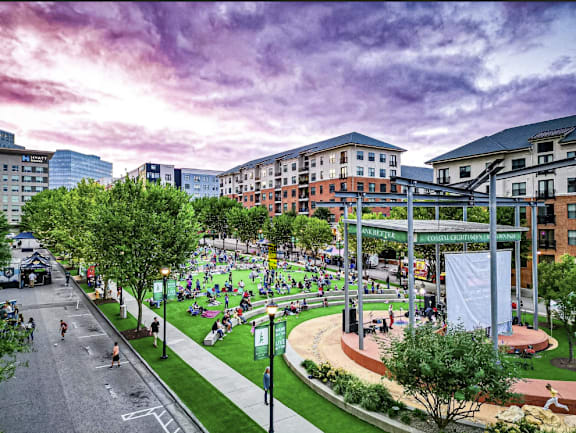 A park with people sitting and walking on the grass and a building in the background.