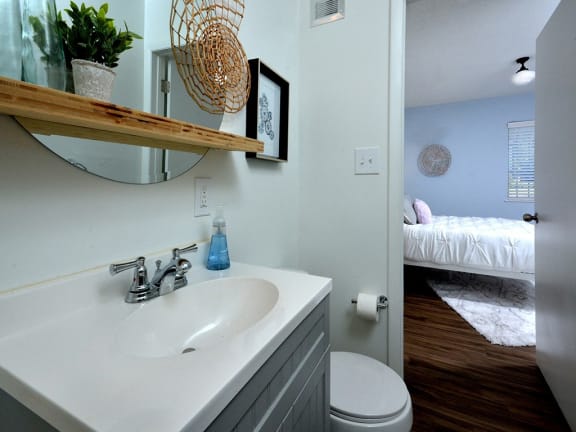a bathroom with a sink and a mirror and a bedroom with a bed at Capital Flats &amp; Magnolia Square Apartments, Raleigh, NC, 27601