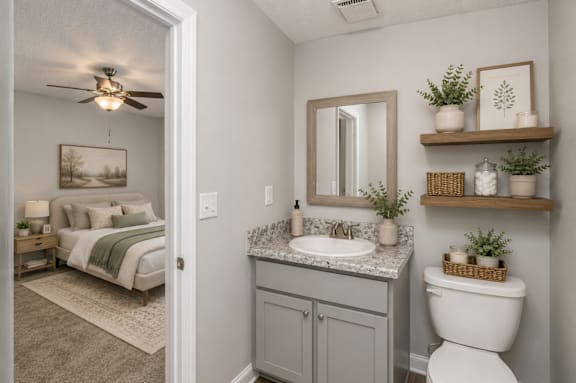 A bathroom with a toilet, sink, and bedroom in the background.
