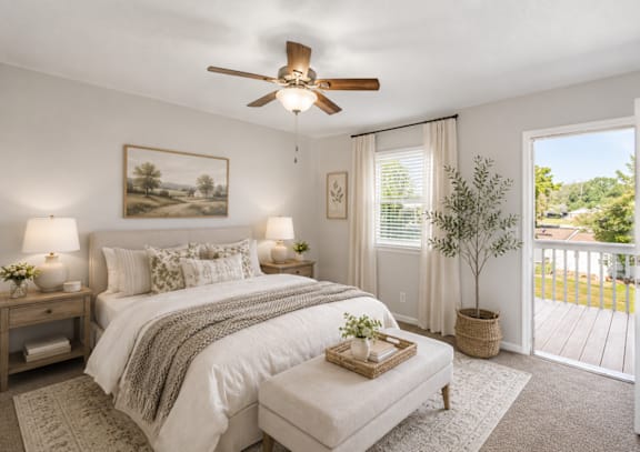A bedroom with a large bed, a ceiling fan, and a view of the backyard through the window.