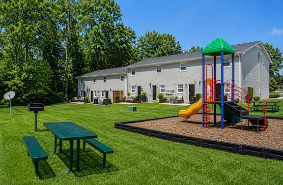 A playground with a green slide and a picnic table in front of a grey building.