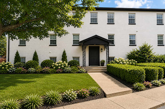 A white building with a black door and windows surrounded by greenery.