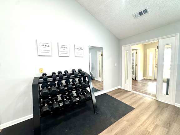 A black dumbbell rack is in the corner of a room with a mirror and three signs on the wall.