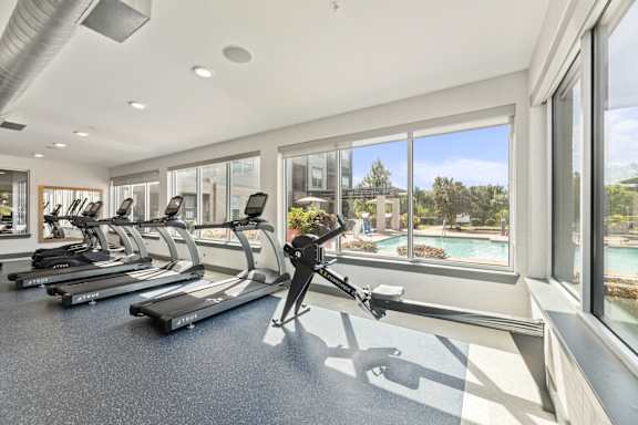 A treadmill in a gym with a view of a pool and trees outside the window.
