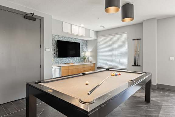 A pool table in a room with a television and a window.