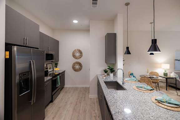 A modern kitchen with a stainless steel refrigerator and a dark grey countertop at Hudson at Renaissance Apartments, North Carolina 28405