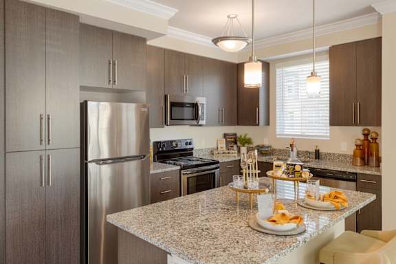 Designer kitchen with dark brown cabinets, granite countertops, kitchen island and stainless appliances; open to the living room and dining room
