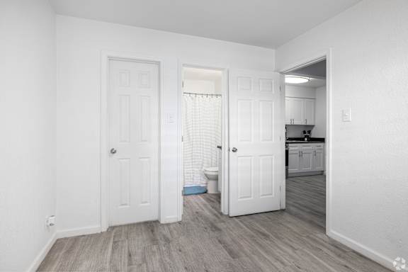 A white room with a door and a hallway leading to a kitchen.