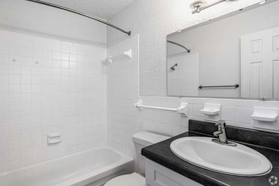 A white tiled bathroom with a black countertop and a white sink.