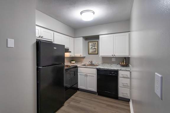 A black refrigerator is in a kitchen with white cabinets in a 1 bedroom, 1 bath 560 square foot apartment at Aspen Village Apartments in the Westwood neighborhood of Cincinnati, OH.
