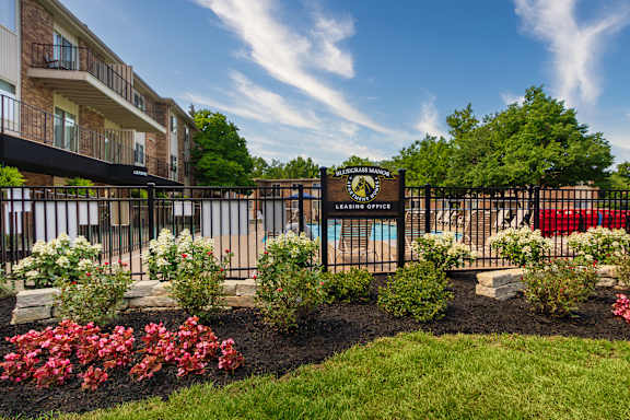 A sign for Blue Gras Manor's Leasing Office is in front of the pool area surrounded by flowers at Blue Grass Manor Apartments in Erlanger, KY.