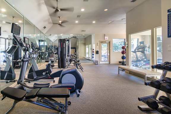 The 24-hour fitness center with treadmills, elliptical machines, and free weights at The Brownstones Townhome Apartments in the Far North Dallas neighborhood of Dallas, TX..