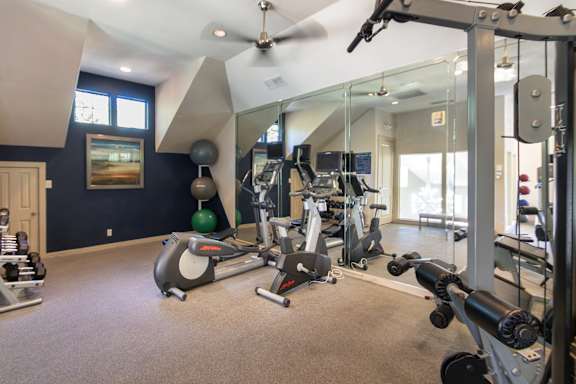 The 24-hour fitness center with treadmills, elliptical machines, and free weights at The Brownstones Townhome Apartments in the Far North Dallas neighborhood of Dallas, TX..