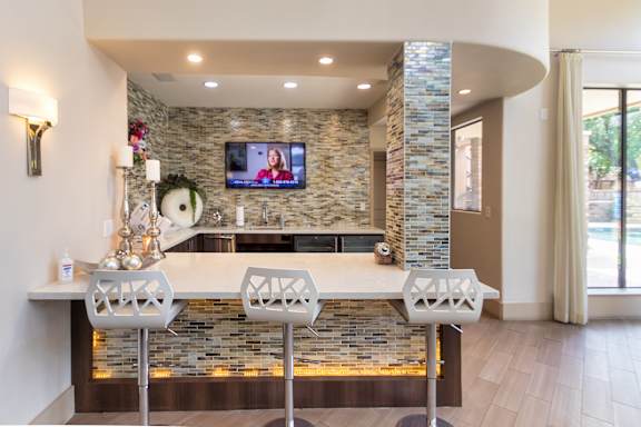 A modern kitchen with a stone backsplash and a TV mounted above the island.