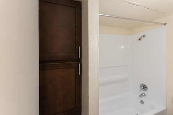 The linen closet and white tub in the bathroom in a 1 bedroom, 1 bath C, 653 sq ft apartment home with hardwoodlike flooring throughout at The Biltmore Apartments located in the Vickery Midtown neighborhood of Dallas, TX.
