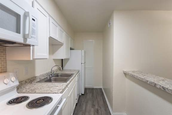 Kitchen with white cabinets and appliances in a 1 bedroom, 1 bath 752 sq ft apartment home with hardwoodlike flooring throughout at The Biltmore Apartments located in the Vickery Midtown neighborhood of Dallas, TX.